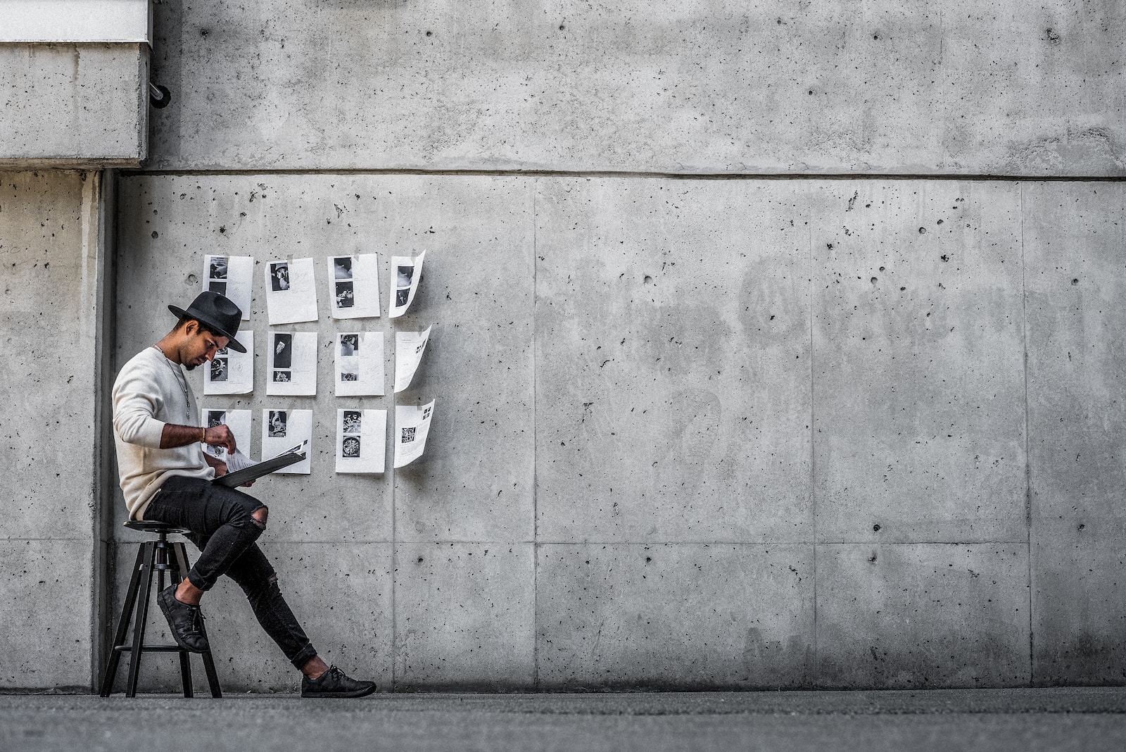 man in black jacket and black pants sitting on concrete wall