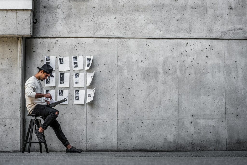 man in black jacket and black pants sitting on concrete wall